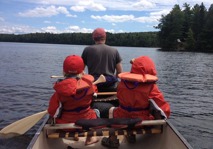 two kids with life vests and a man in a canoe on the water