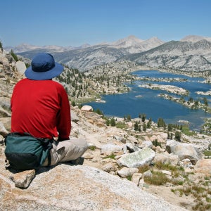 A man sits atop an overlook, gazing below at a panorama of Marie Lake and several Sierra Nevada peaks.