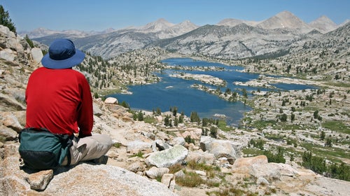 A man sits atop an overlook, gazing below at a panorama of Marie Lake and several Sierra Nevada peaks.