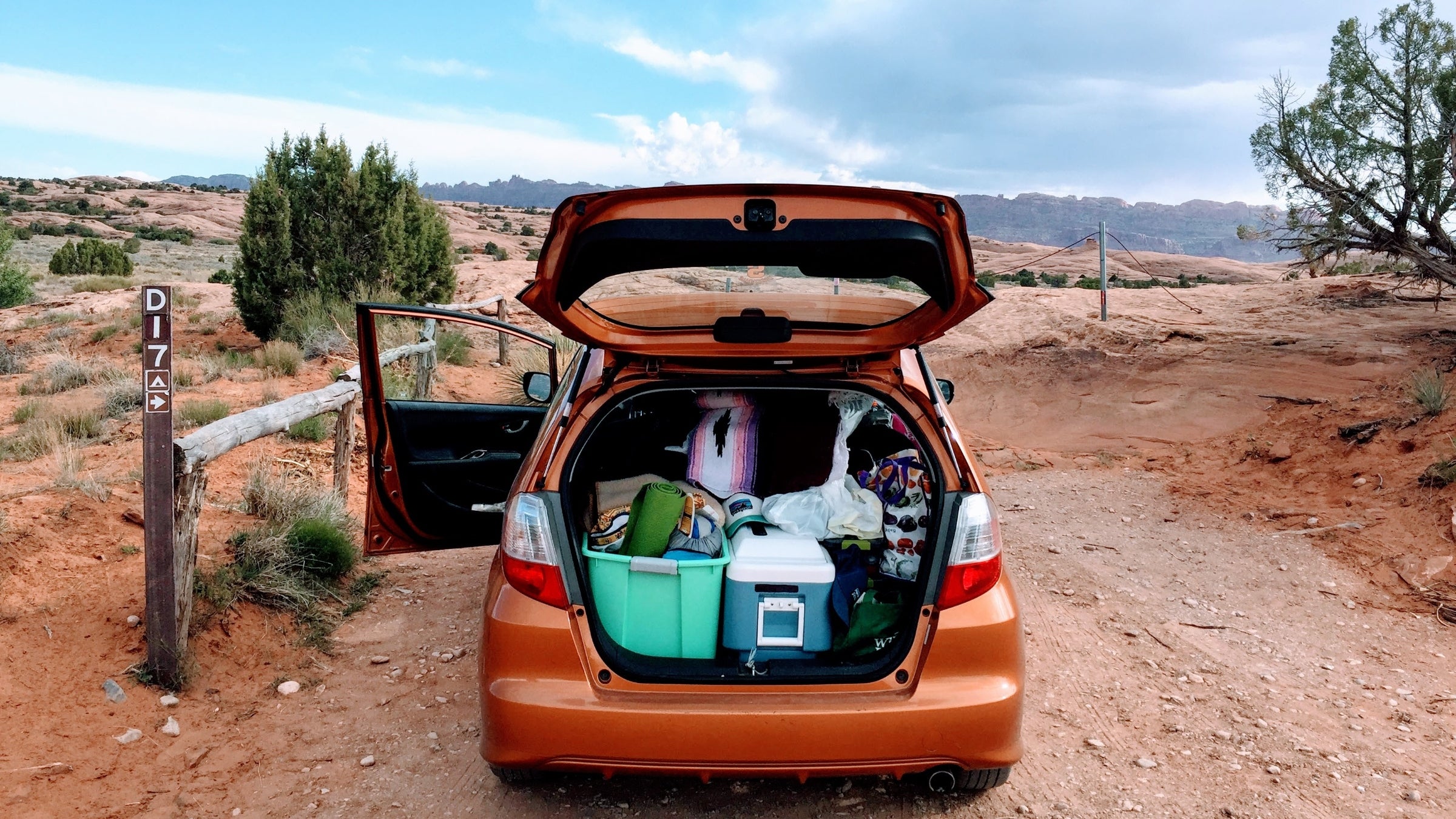 An open car trunk packed with camping gear on a rural desert road.