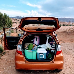 An open car trunk packed with camping gear on a rural desert road.