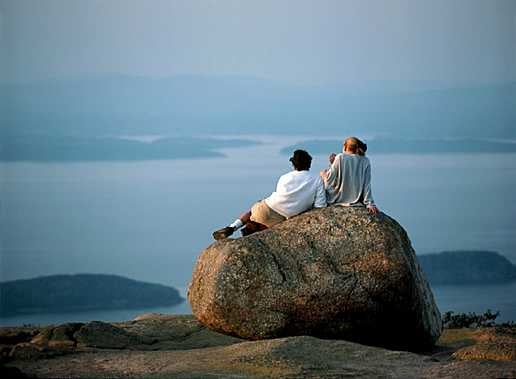 two people sitting on a rock overlooking the ocean