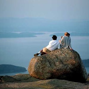 two people sitting on a rock overlooking the ocean