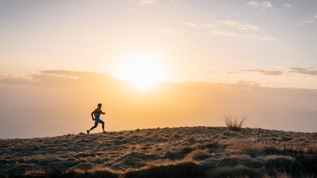 A man running uphill towards the sunset