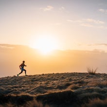 A man running uphill towards the sunset