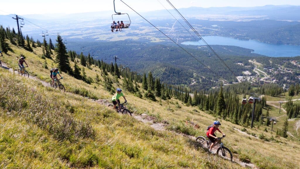 A family mountain-bikes downhill above the town of Whitefish, Montana, with a spectacular view of Flathead Lake.