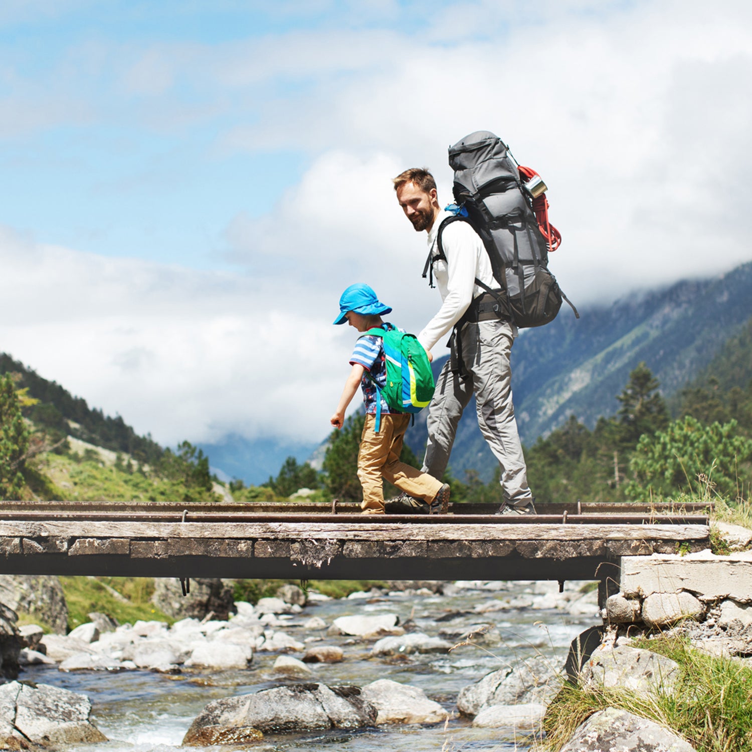 Father and young son walking across bridge over mountain stream