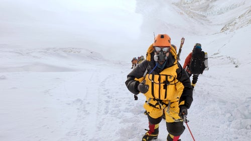A climber in an oxygen mask giving a thumbs up on Mount Everest