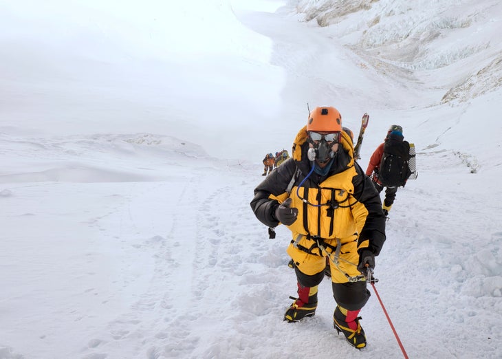 A climber in an oxygen mask giving a thumbs up on Mount Everest