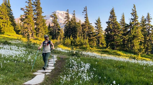 The author hikes along a hillside path amid white wildflowers with Mount Rainier, Washington, behind her in the distance.