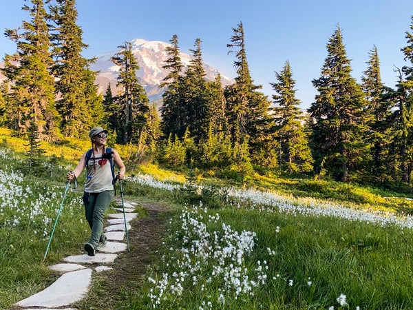 The author hikes along a hillside path amid white wildflowers with Mount Rainier, Washington, behind her in the distance.