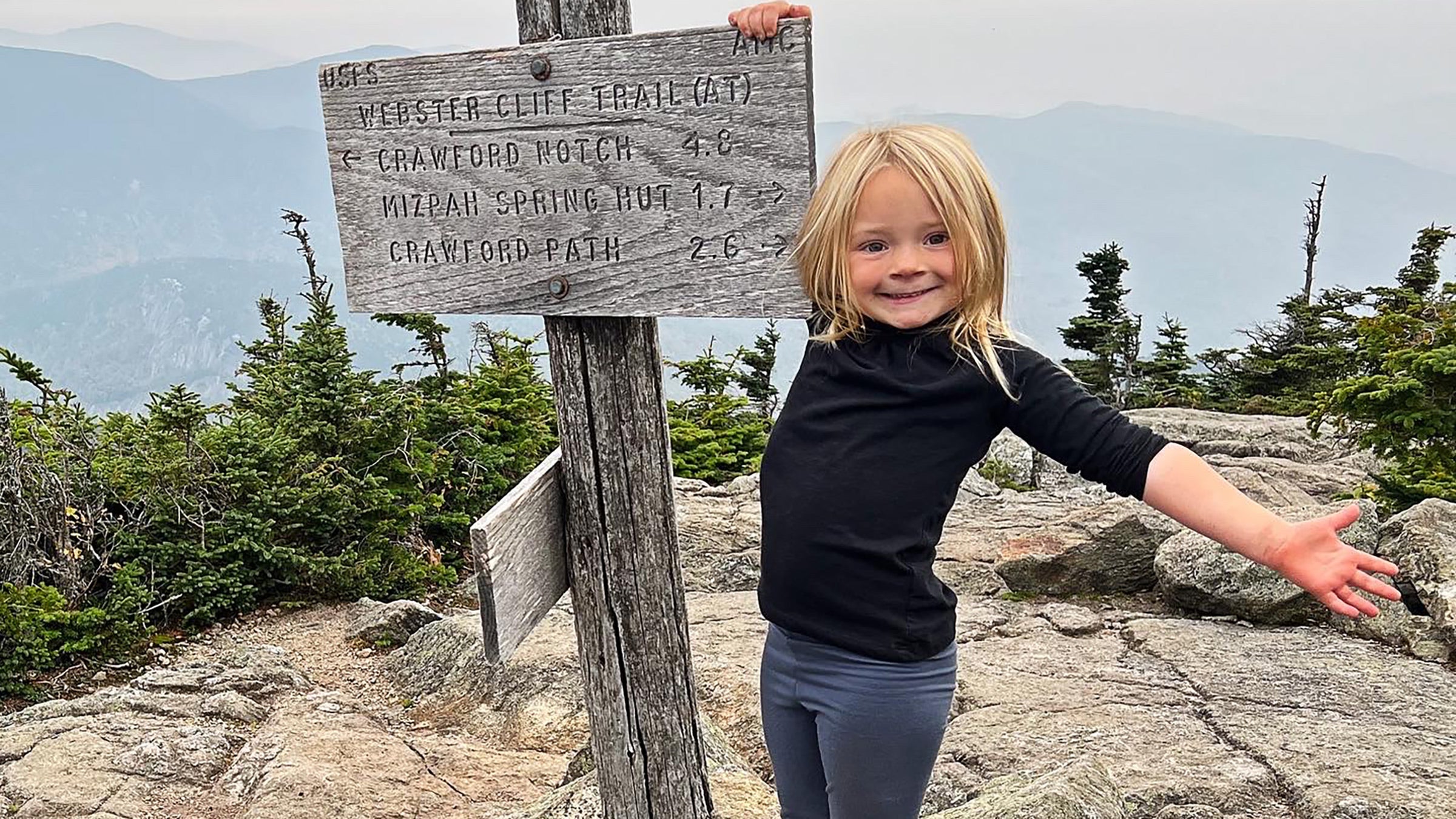 A small child stands on top of a mountain in New England