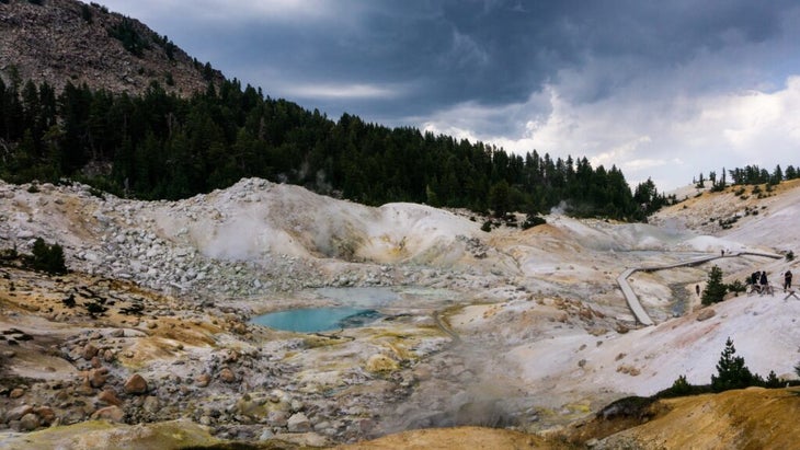 The landscape of Lassen National Park’s Bumpass Hell Trail is otherworldly, with white and yellow hills and a turquoise-colored pool.