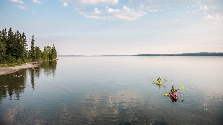 Two people paddle kayaks on Clear Lake, Riding Mountain National Park.