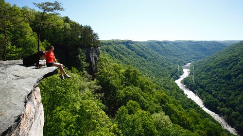 A girl and her dog sit on a stone bluff overlooking the New River of West Virginia.
