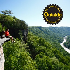 A girl and her dog sit on a stone bluff overlooking the New River of West Virginia.