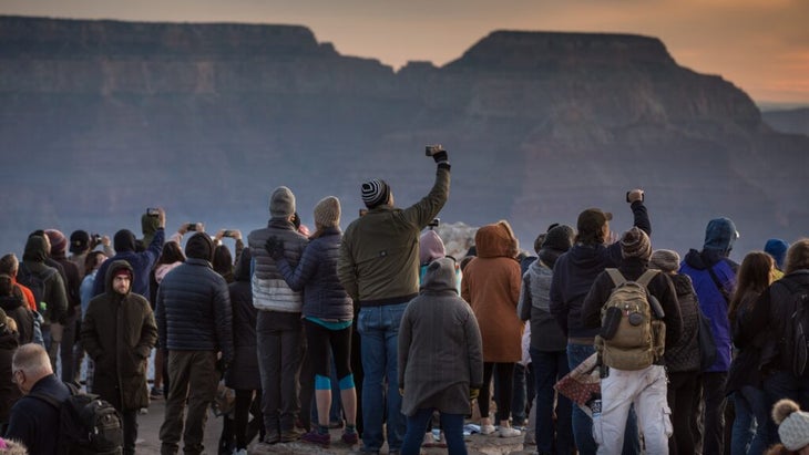 A large group of tourists gather at the Grand Canyon's South Rim to take photos of sunrise.