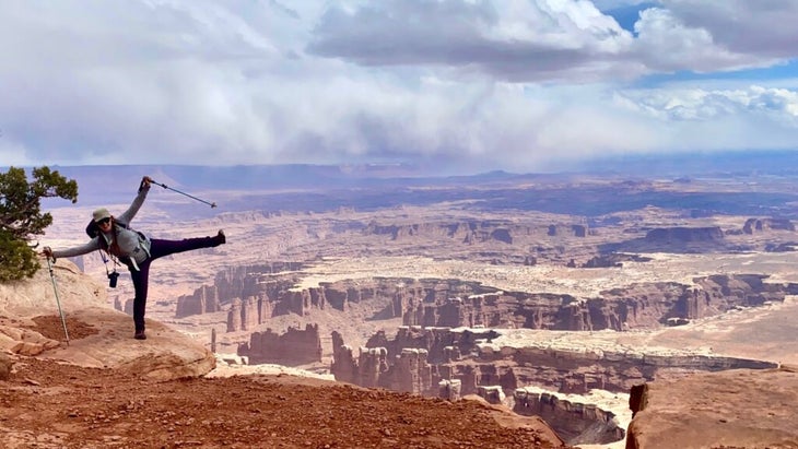 The author holding hiking poles jokes like she's about to cartwheel into the huge canyon below Grand View Point in Canyonlands National Park.