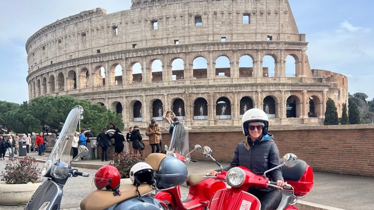 The author sitting atop a red Vespa with the Roman Colosseum behind her.