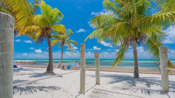 Two women shake out beach blankets along the shore and under the palms in Key West, Florida, with a view of turquoise waters