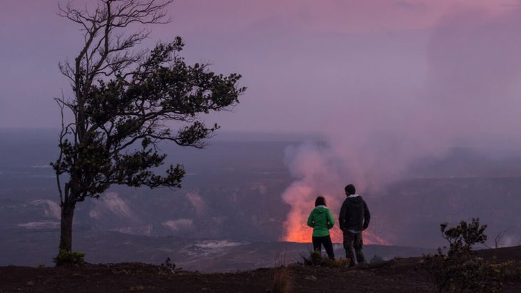 A couple stands in the twilight looking at the glow of Kilauea, on Hawaii Island.