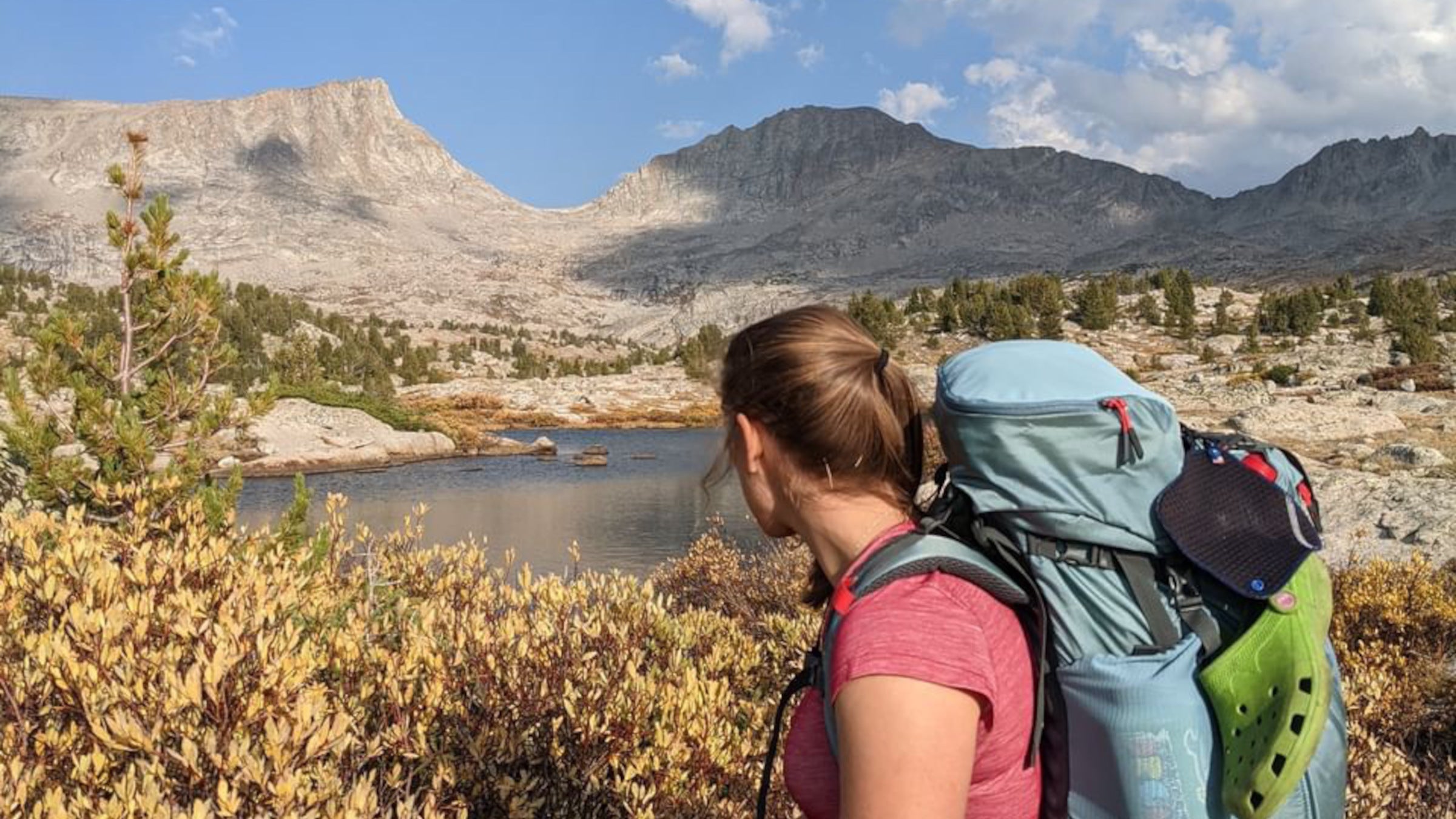 A female backpacker stands in front of a mountainous backdrop