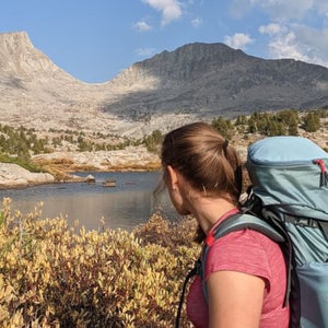 A female backpacker stands in front of a mountainous backdrop