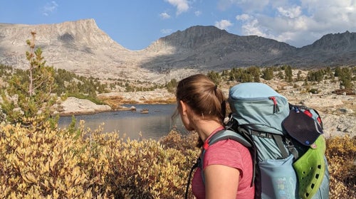A female backpacker stands in front of a mountainous backdrop