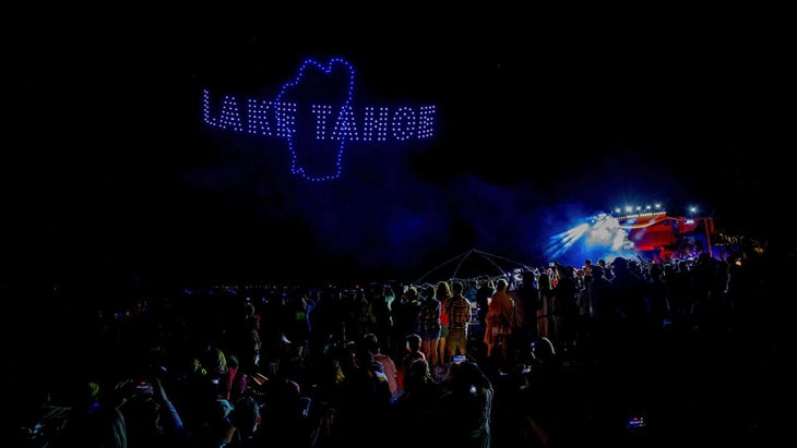 "Lake Tahoe" illunimated in night sky during a drone fireworks show with a crowd of people in foreground.