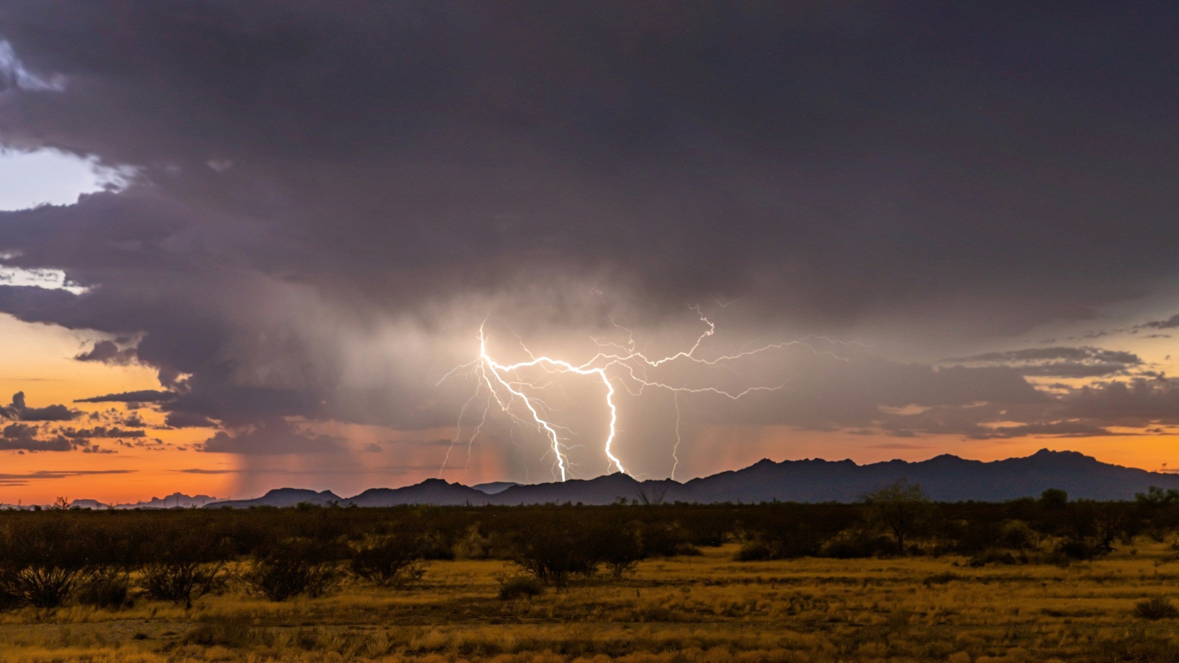 Two bolts of lighting glow on a dark cloudy background over the mountains of the Western U.S.