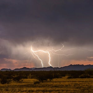 Two bolts of lighting glow on a dark cloudy background over the mountains of the Western U.S.