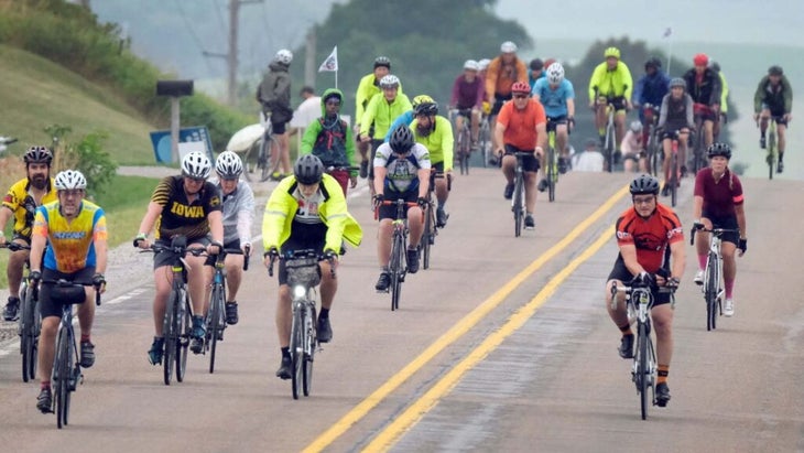 A group of riders coast down a two-lane road that's closed to traffic. One man's jersey reads "Iowa."