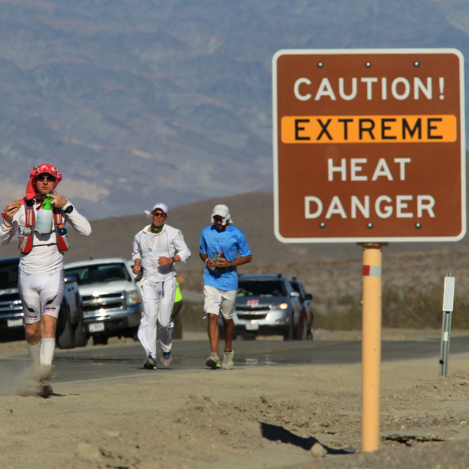 Four male runners passing a heat danger sign at the Badwater 135 ultramarathon in Death Valley