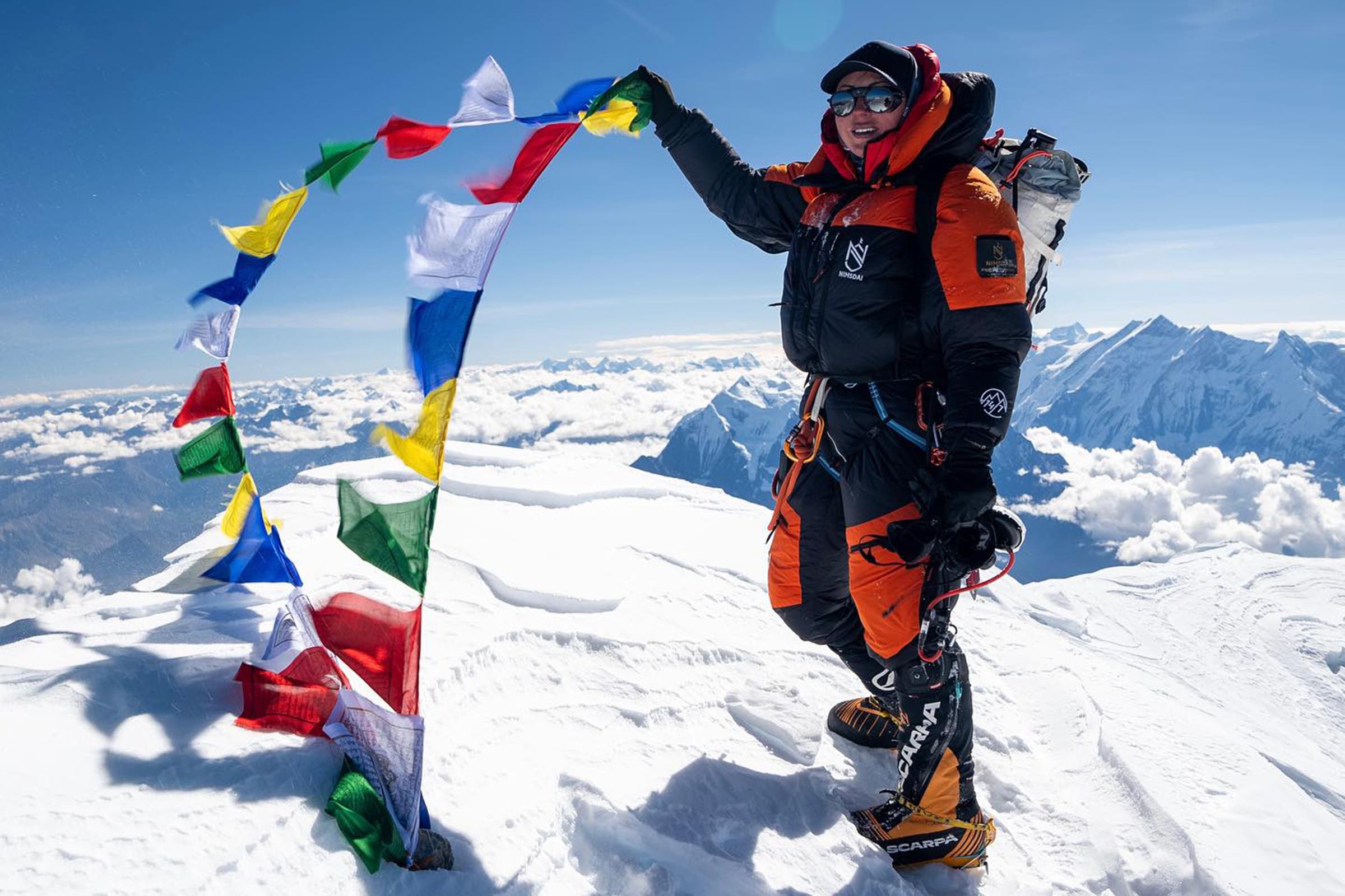A woman on top of a mountain holds prayer flags