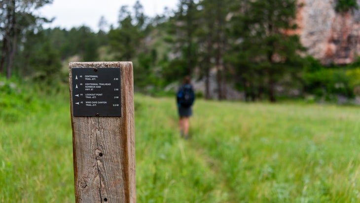 Centennial Trail Junction Sign Post with Woman Hiking in Distance