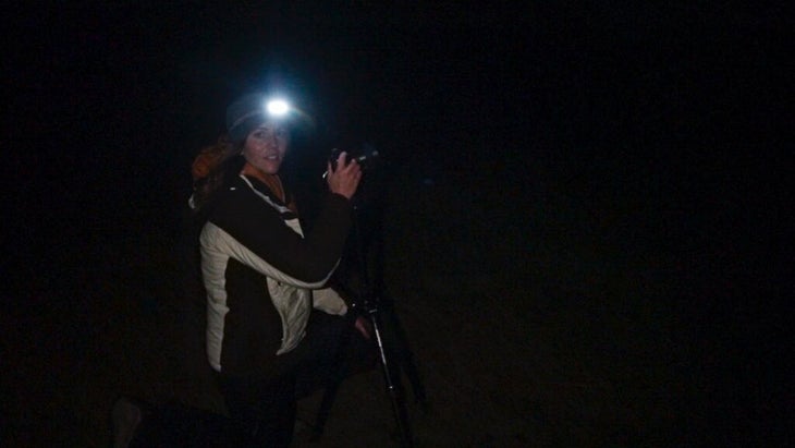 The author in the dark outside at night, wearing a headlamp and setting up her camera equipment.