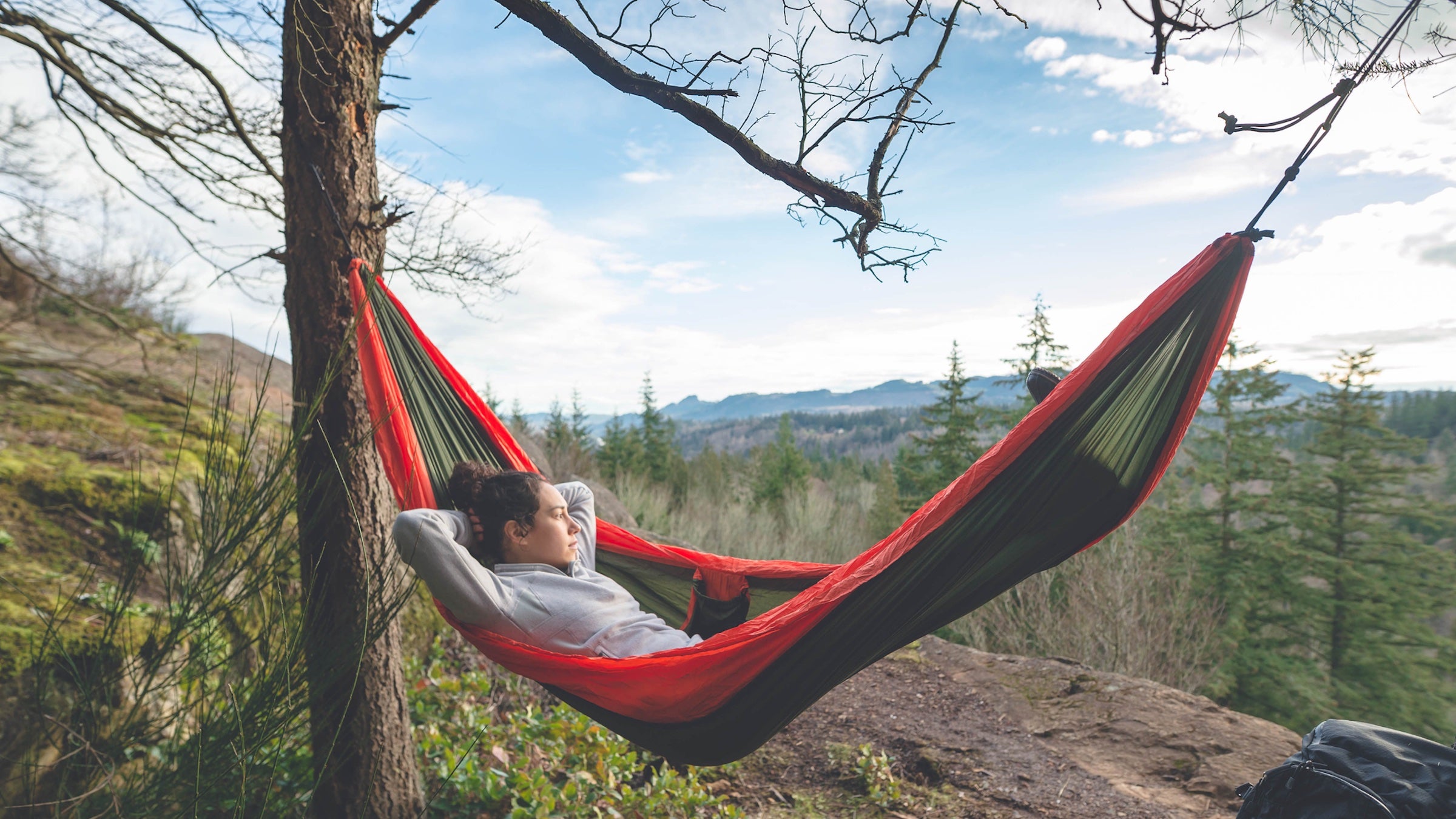 a woman relaxing in a red hammock (training less!) in the mountains