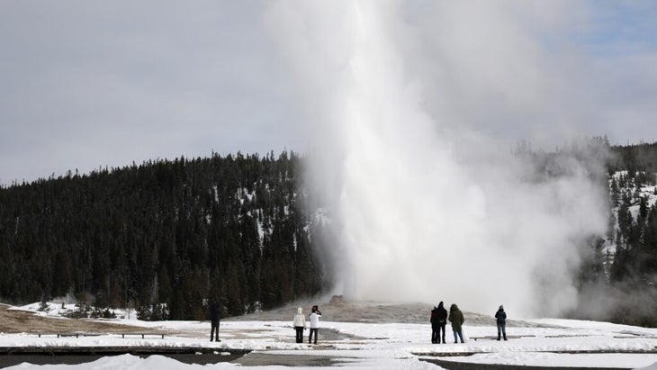 A few people mingle around Old Faithful in winter. 