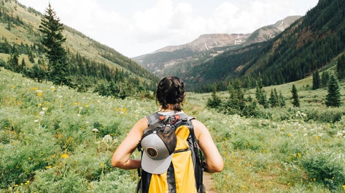 A woman wearing a yellow backpack hikes through a mountainous valley in Crested Butte, Colorado.