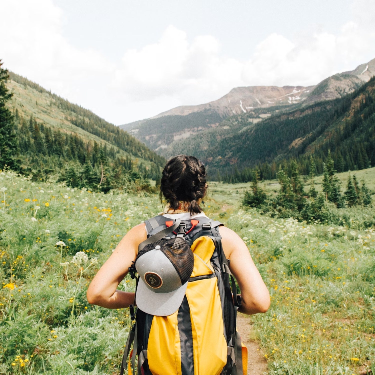 A woman wearing a yellow backpack hikes through a mountainous valley in Crested Butte, Colorado.