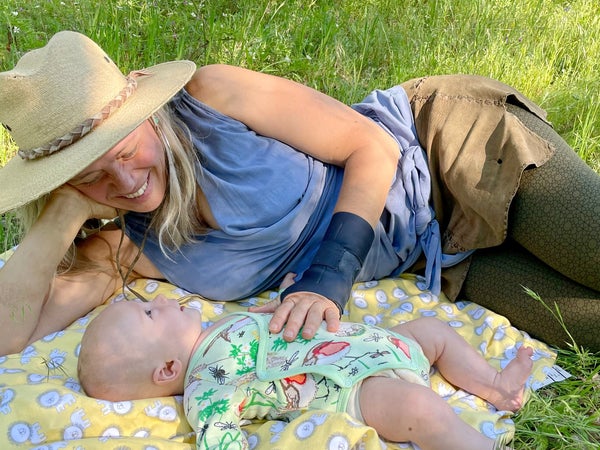 Woniya Thibeault lying on a blanket on the grass next to her infant son.