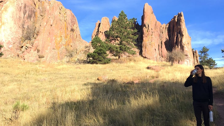 a person standing in dry grass in front of a cliff