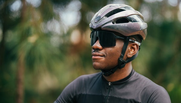 young man wearing a bike helmet and sunglasses takes a break during a ride against a leafy background