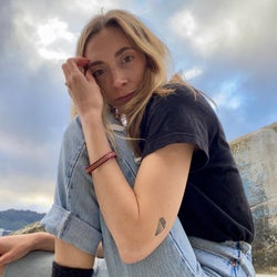 A blonde woman sits outside wearing a black t-shirt and cuffed blue jeans.