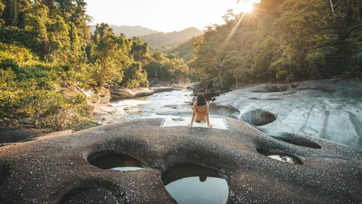 A woman sits on a blanket overlooking the Babinda boulders swimming pools near Cairns, Queensland.