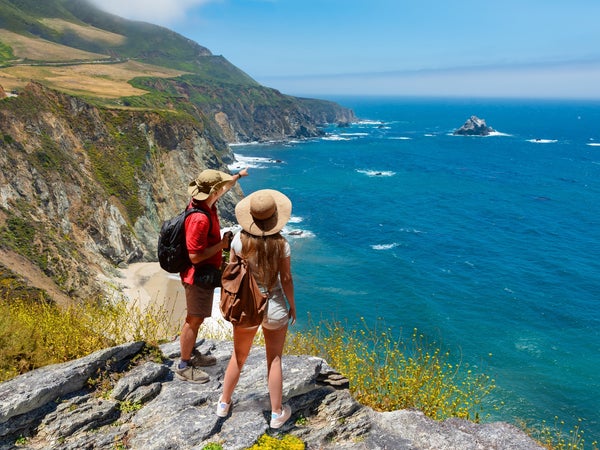 A couple with backpacks hiking near the coast of Big Sur, California, pauses to look at over the Pacific Ocean.