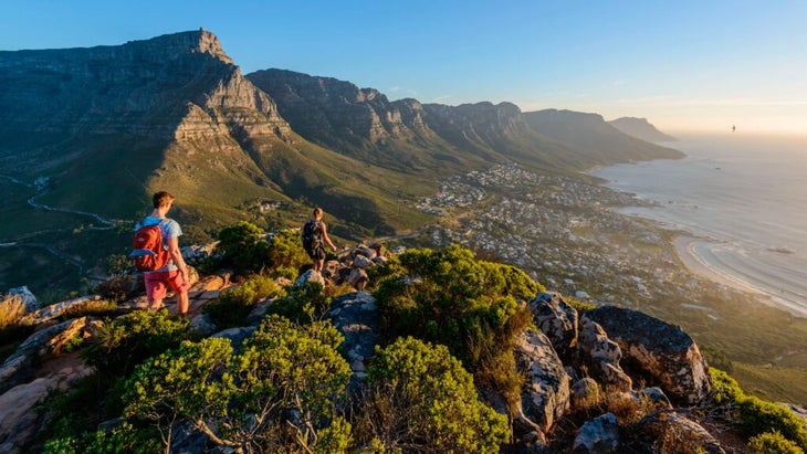 Two hikers rambling along a trail with views of Table Mountain and the 12 Apostles viewed from Lion's Head, Cape Town.