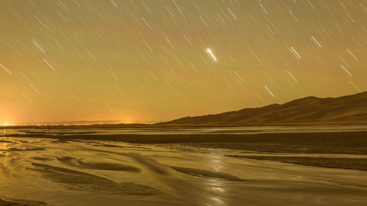 A glowing night sky with a shooting star over Colorado’s Great Sand Dunes National Park and Medano Creek