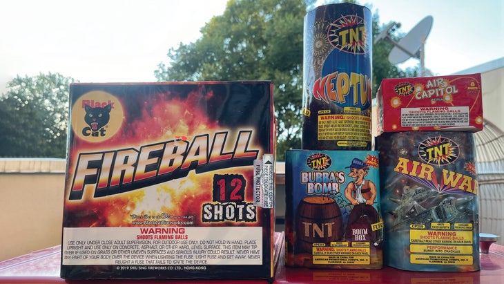 Various types of consumer fireworks stacked on an outdoor table