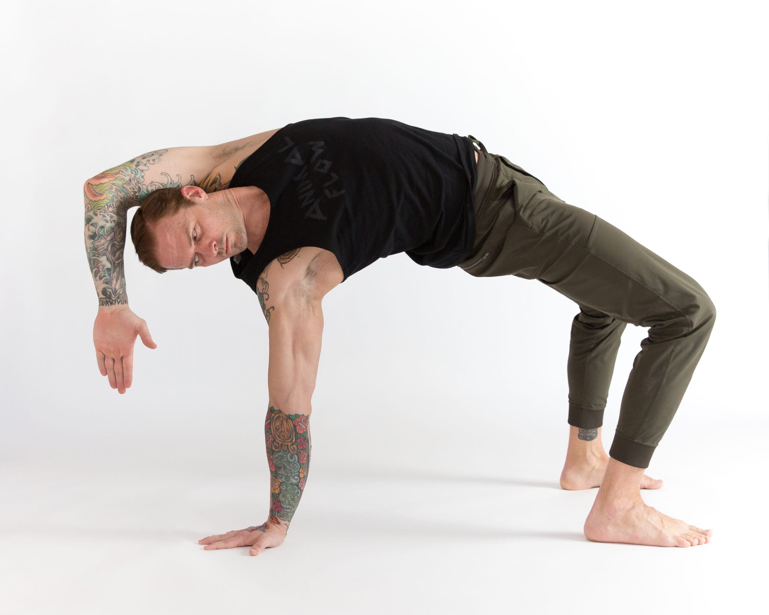 Man in crab reach. He is in a supine position with knees bent, back arched, right hand on the ground with a straight arm, and left arm bent at the elbow, with the left hand pointing toward the ground.